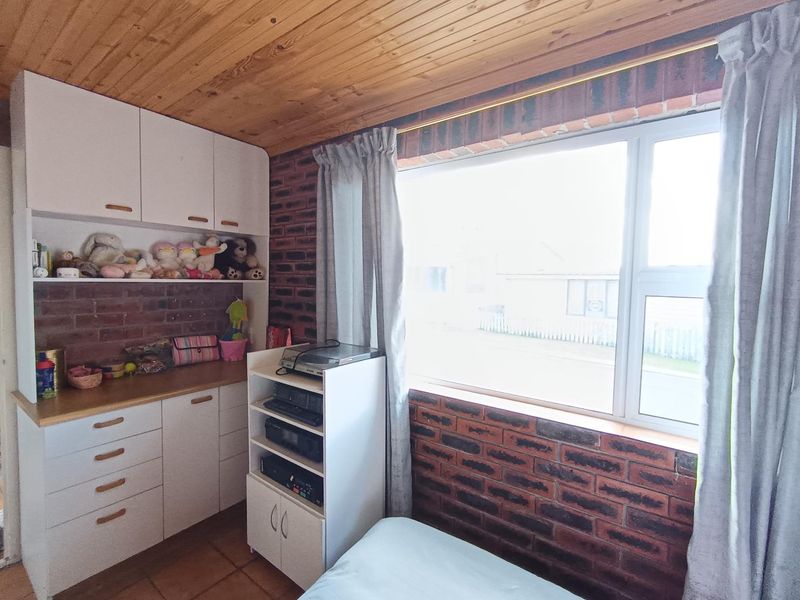 A bedroom featuring exposed brick walls, timber ceiling paneling, built-in cabinetry, and large windows allowing for natural light.