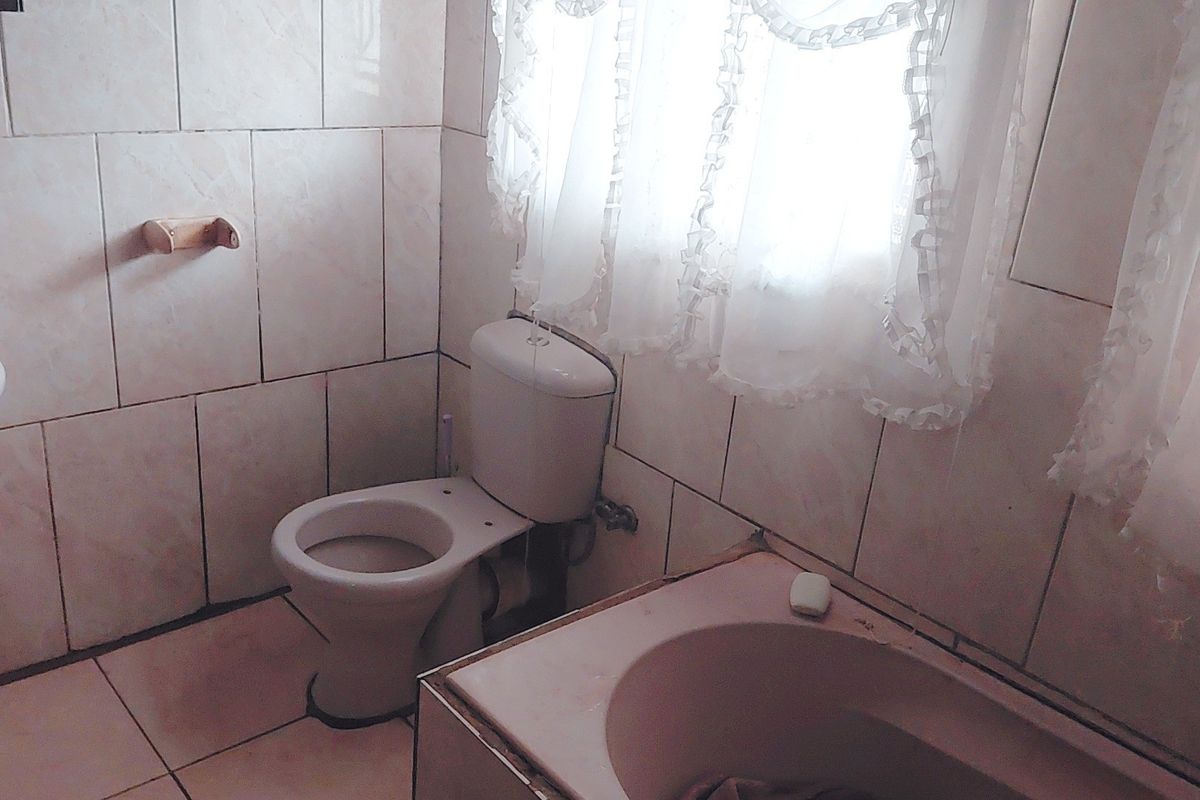 A dated bathroom featuring a standard toilet, bathtub, and washbasin with full-height wall tiling and floor tiles.