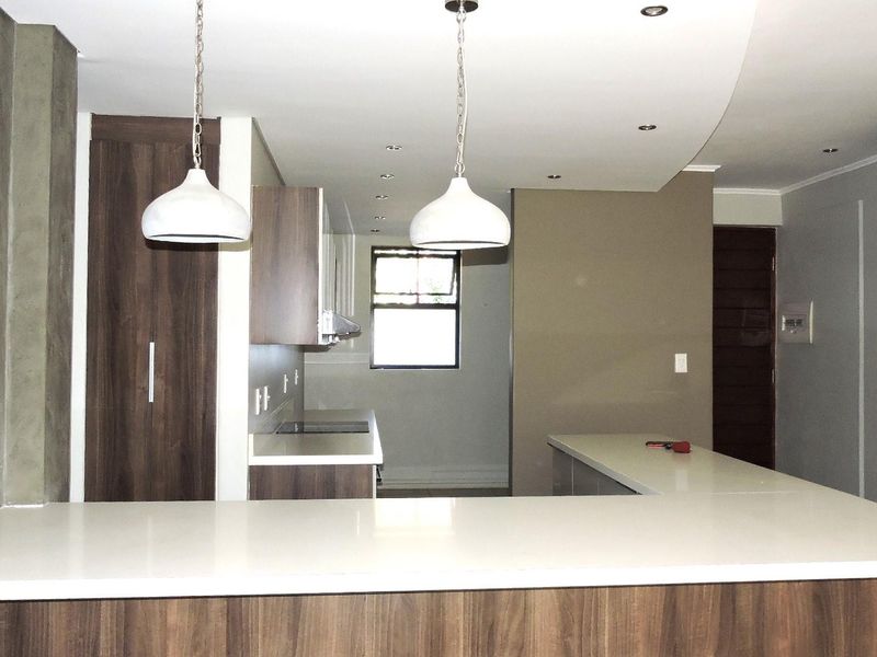 Modern open-plan kitchen featuring sleek cabinetry, stone countertops, integrated hob, and stylish pendant lighting, creating a functional and contemporary living space.