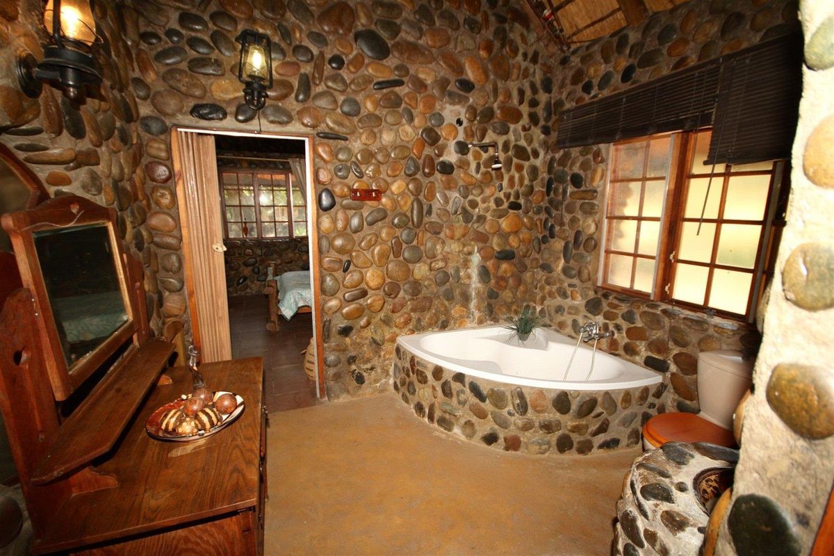 A rustic bathroom featuring unique natural stone wall cladding, a built-in corner bathtub, and timber-framed windows.