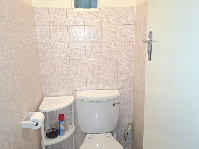 A compact bathroom featuring a standard toilet and dated ceramic wall tiling, providing a functional space with potential for modern updates.
