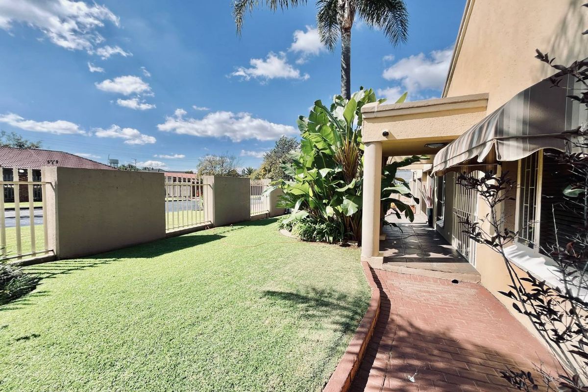 A well-maintained exterior side garden featuring a paved walkway, covered patio area, and perimeter walling with metal fencing.