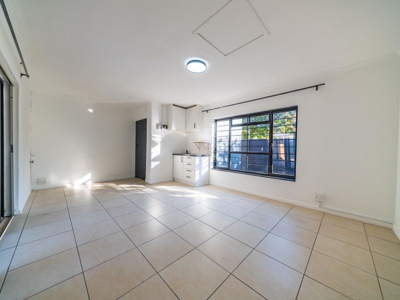 An open-plan living area featuring tiled flooring, a sliding door to the exterior, and a compact kitchenette with built-in cabinetry.
