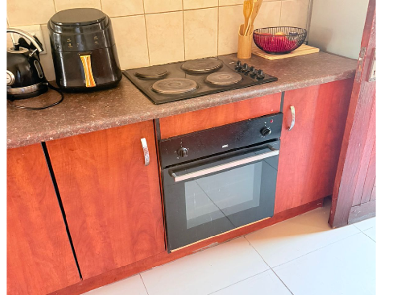 A functional kitchen area featuring a built-in oven, electric hob, laminate cabinetry, and tiled backsplash with neutral floor tiling.