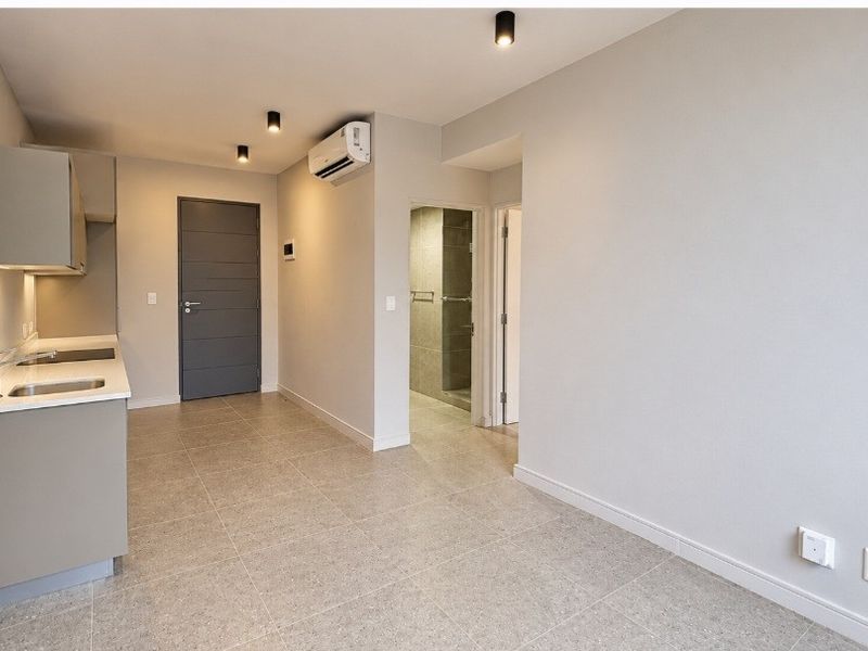 Modern open-plan living area featuring a sleek kitchenette with stone countertops, tiled flooring, recessed lighting, and an integrated air conditioning unit.