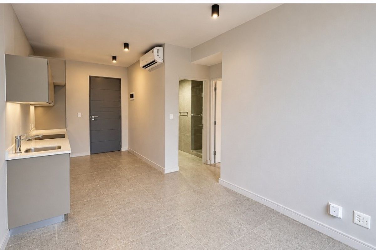 Modern open-plan living area featuring a sleek kitchenette with stone countertops, tiled flooring, recessed lighting, and an integrated air conditioning unit.