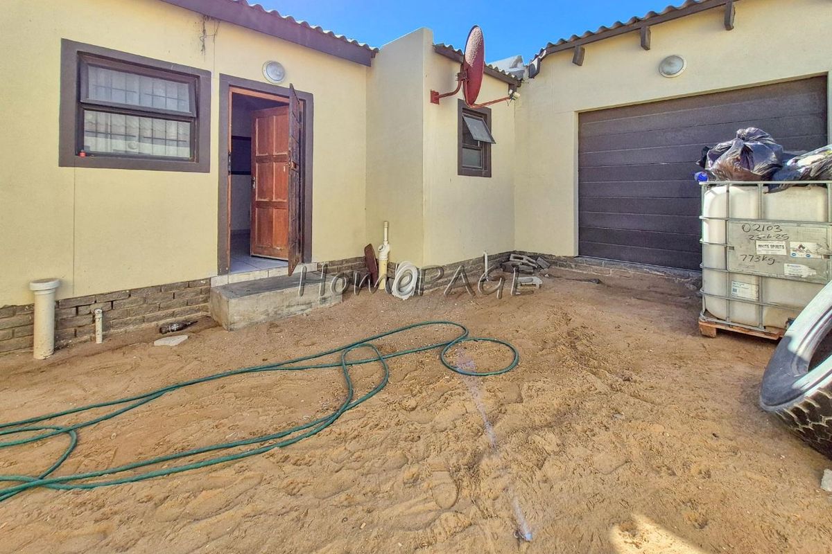 Rear exterior view of the property featuring a garage door, entrance door, and an unpaved courtyard area.