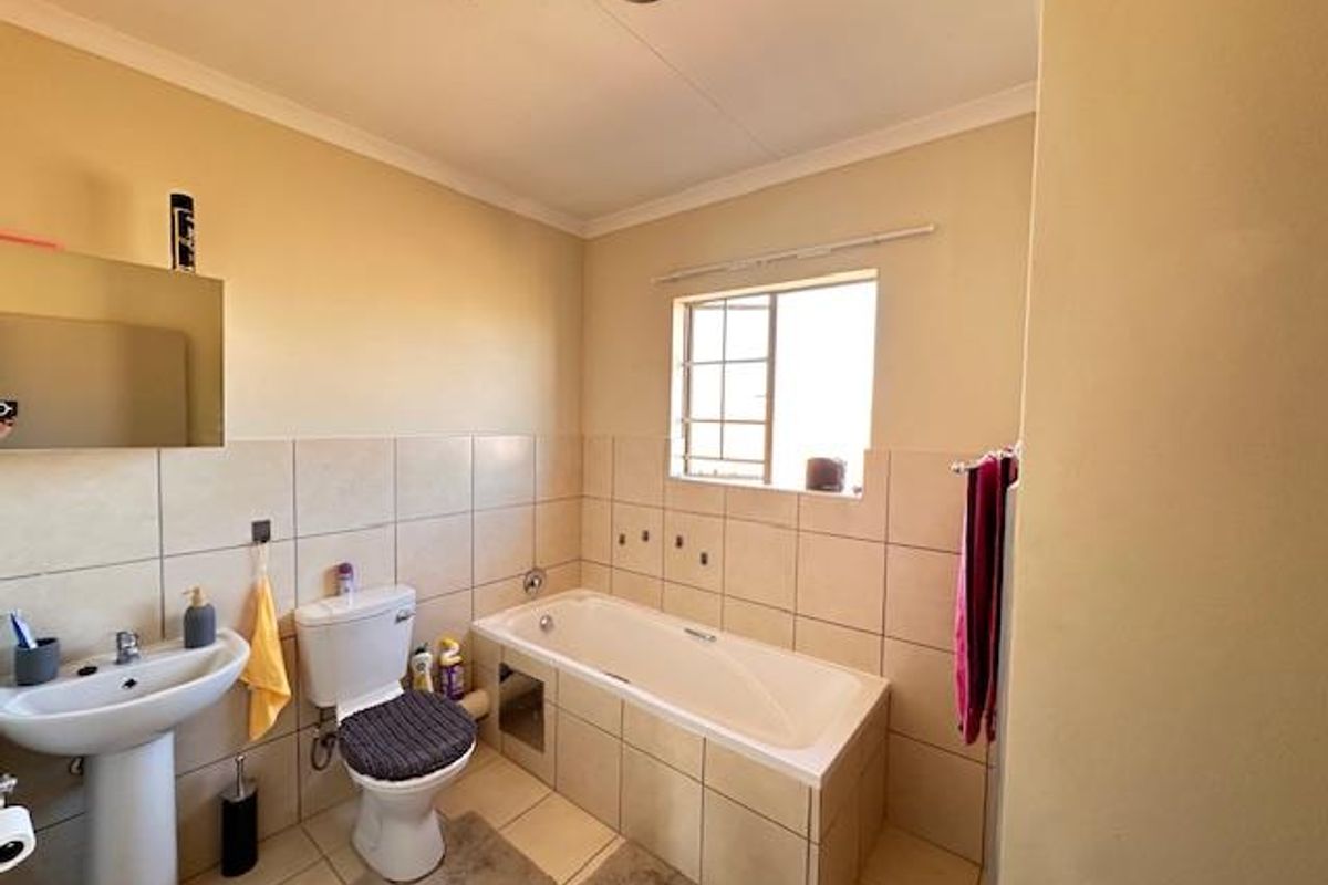 A functional bathroom featuring a pedestal sink, a built-in bathtub with tiled surround, and a window with security bars.
