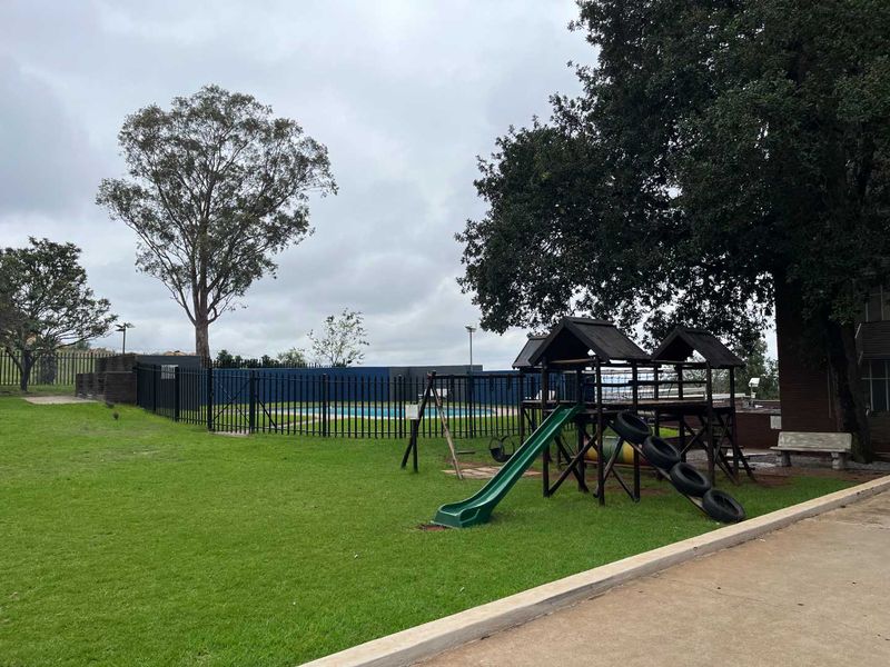 Communal outdoor area featuring a swimming pool enclosed by metal fencing, set within a landscaped garden with a paved walkway.