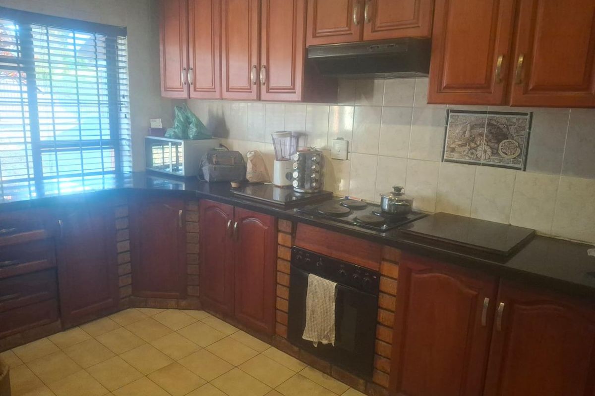 A functional kitchen featuring wooden cabinetry, granite countertops, built-in oven, and electric hob with a tiled backsplash.