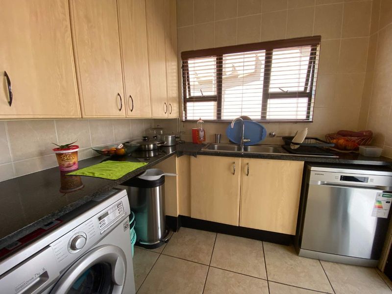 A functional scullery area featuring laminate cabinetry, granite countertops, a double basin sink, and tiled finishes, providing practical utility space.