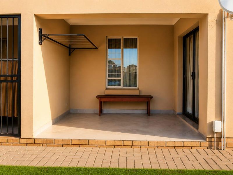 A clean, covered patio area featuring tiled flooring, a wall-mounted drying rack, and secure access via a sliding glass door and security gate.