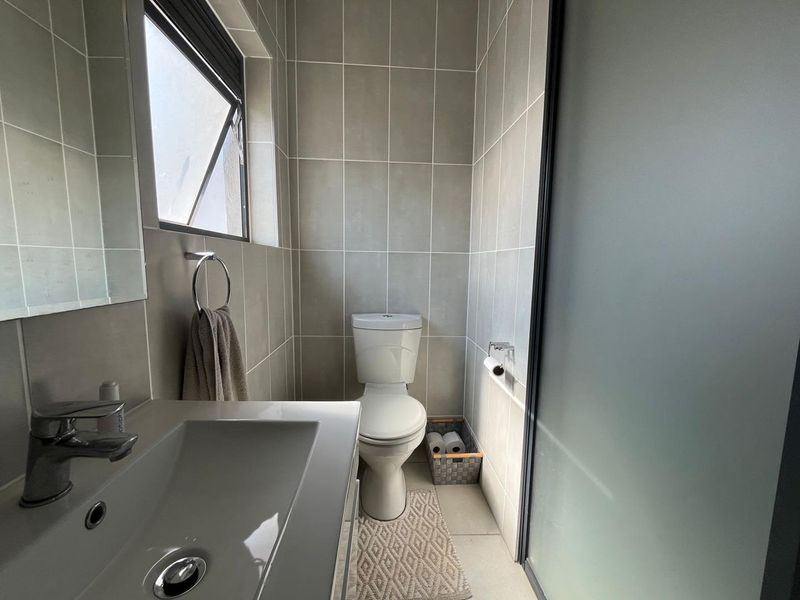 A modern, compact bathroom featuring neutral wall tiles, a vanity basin with a mixer tap, a toilet, and a frosted glass door.