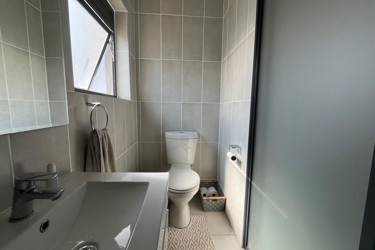 A modern, compact bathroom featuring neutral wall tiles, a vanity basin with a mixer tap, a toilet, and a frosted glass door.