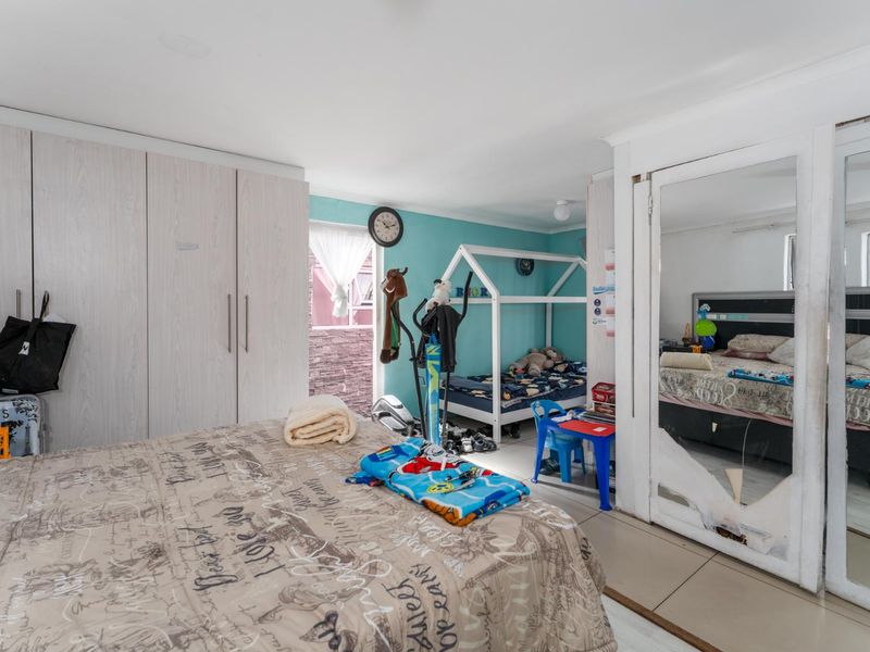 Spacious bedroom featuring built-in cupboards, tiled flooring, and a large mirrored sliding door with visible damage.