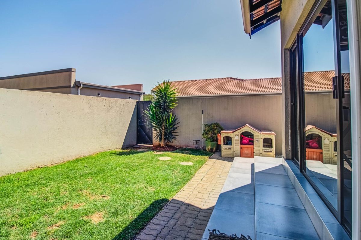 A private rear garden featuring a paved walkway, a small lawn area, and a tiled patio accessible through large sliding glass doors.