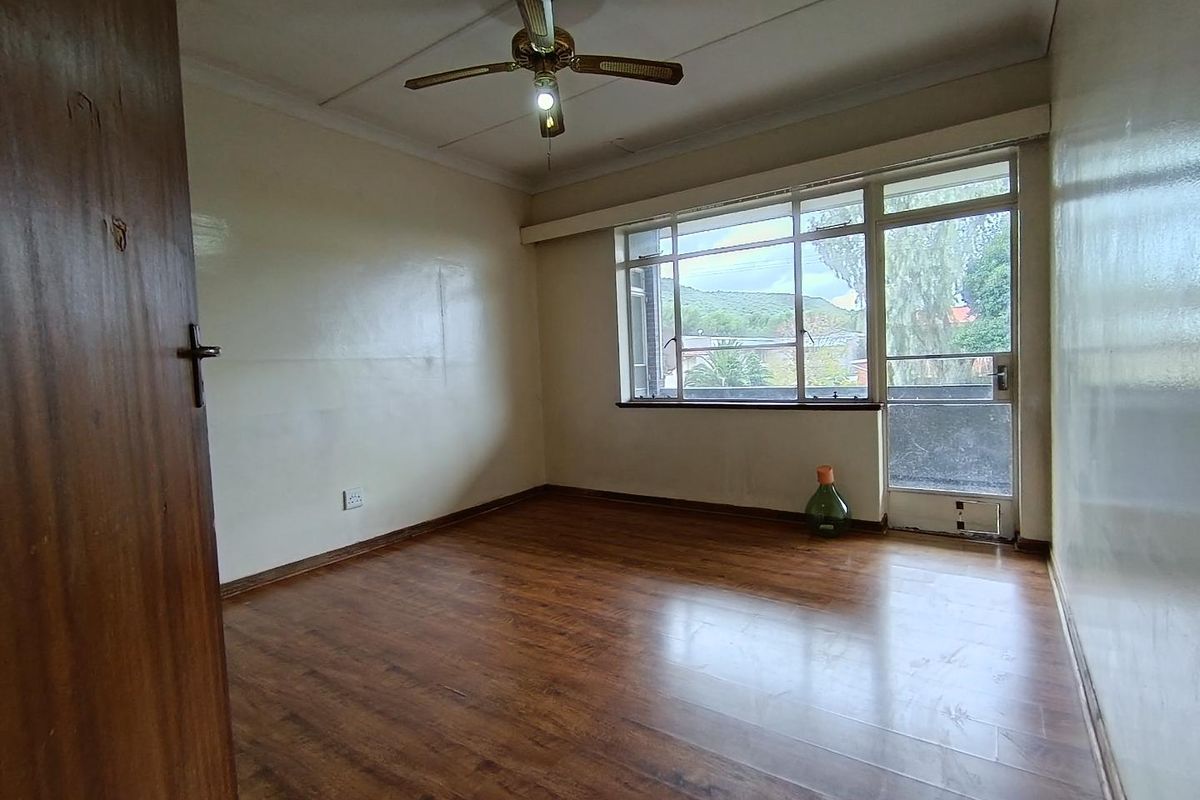 A bright, empty bedroom featuring wood-look laminate flooring, a ceiling fan, and large windows providing natural light and access to a balcony.