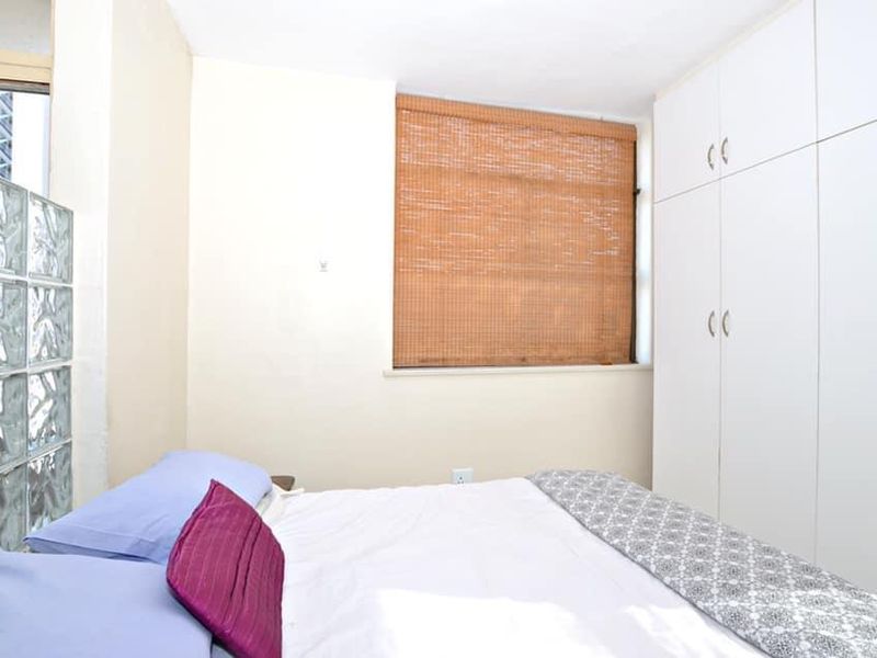 Bedroom featuring built-in white cupboards, a decorative glass block partition, and a bamboo roller blind.