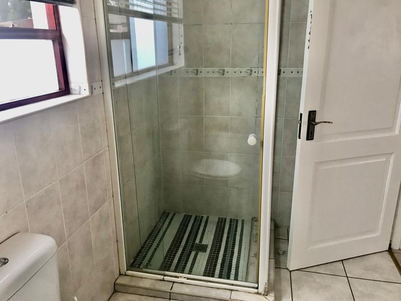 A functional bathroom featuring a glass-enclosed shower with mosaic floor tiling and neutral wall tiles, showing signs of standard wear.