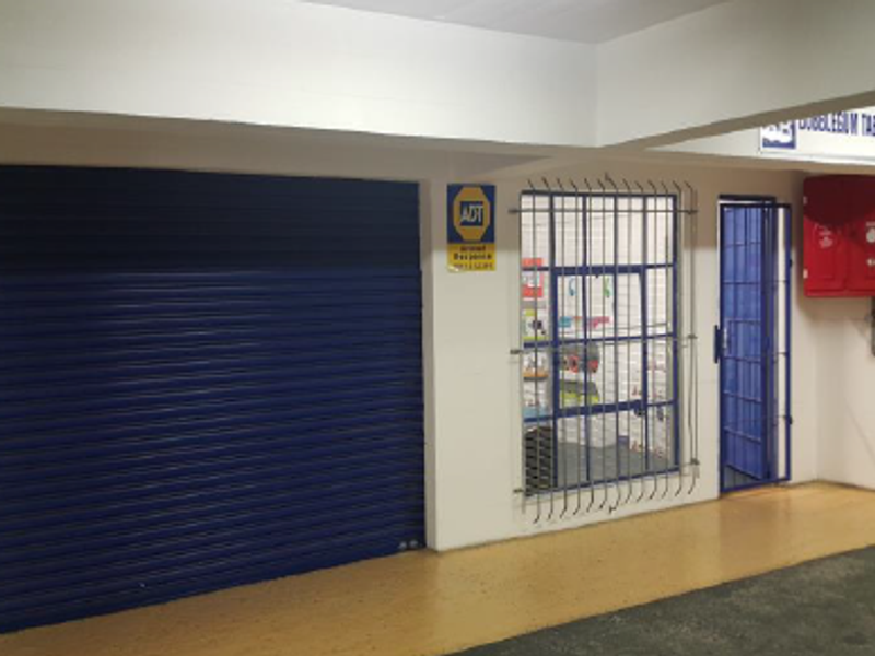 Industrial garage space featuring a secure roller shutter door, security-barred window, and wall-mounted fire safety equipment.