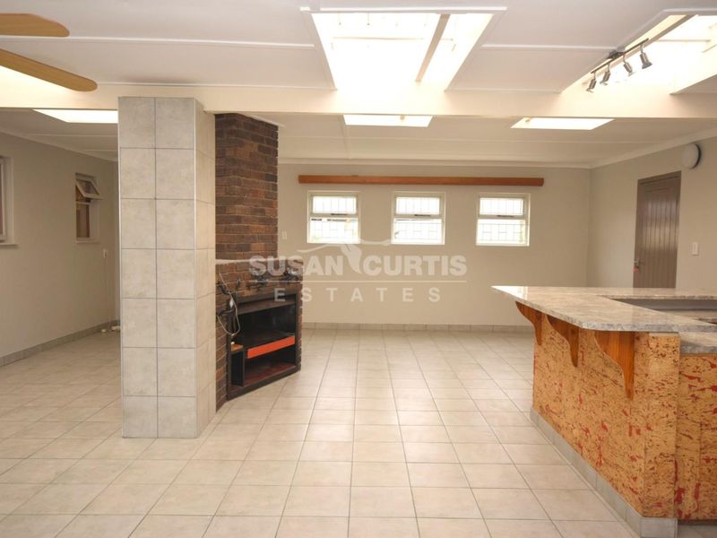 Spacious open-plan living area featuring a built-in brick braai, tiled flooring, breakfast bar, and natural light from overhead skylights.
