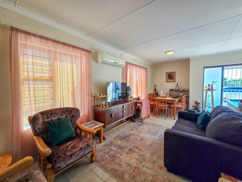 Open-plan living and dining area featuring tiled flooring, a wall-mounted air conditioning unit, and access to an outdoor space via a sliding glass door.