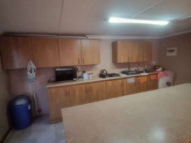 A functional kitchen area featuring wooden cabinetry, laminate countertops, a gas hob, and a stainless steel sink, requiring cosmetic updates.