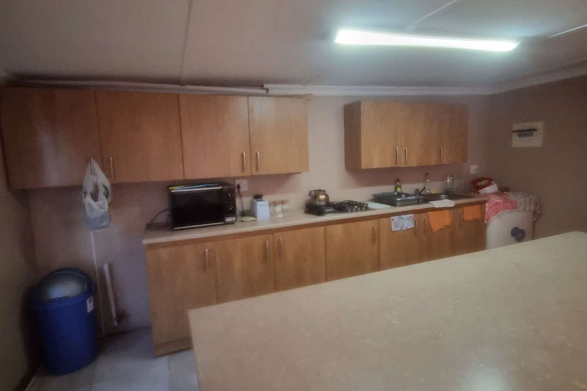 A functional kitchen area featuring wooden cabinetry, laminate countertops, a gas hob, and a stainless steel sink, requiring cosmetic updates.