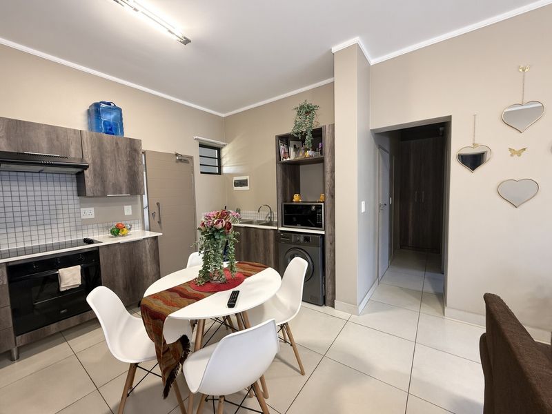 Open-plan kitchen and dining area featuring modern wood-finish cabinetry, built-in appliances, tiled flooring, and direct access to a hallway.