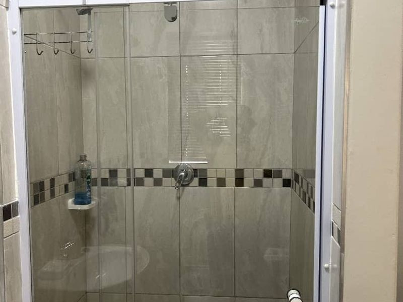 A clean bathroom shower enclosure featuring neutral wall tiles with a decorative mosaic border and a glass door.