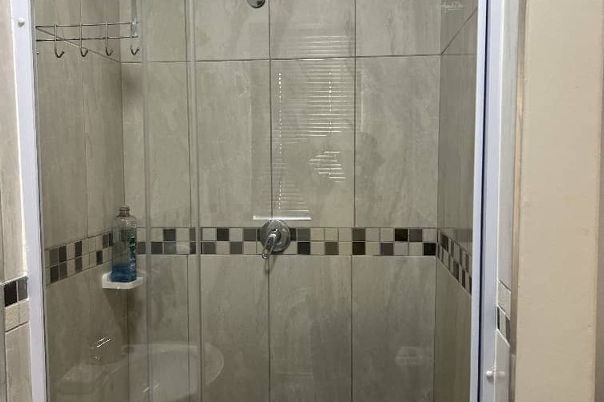 A clean bathroom shower enclosure featuring neutral wall tiles with a decorative mosaic border and a glass door.