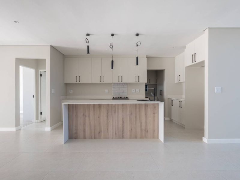 Modern, minimalist kitchen featuring a central island with wood-look finish, stone countertops, built-in cabinetry, and sleek pendant lighting in an open-plan layout.