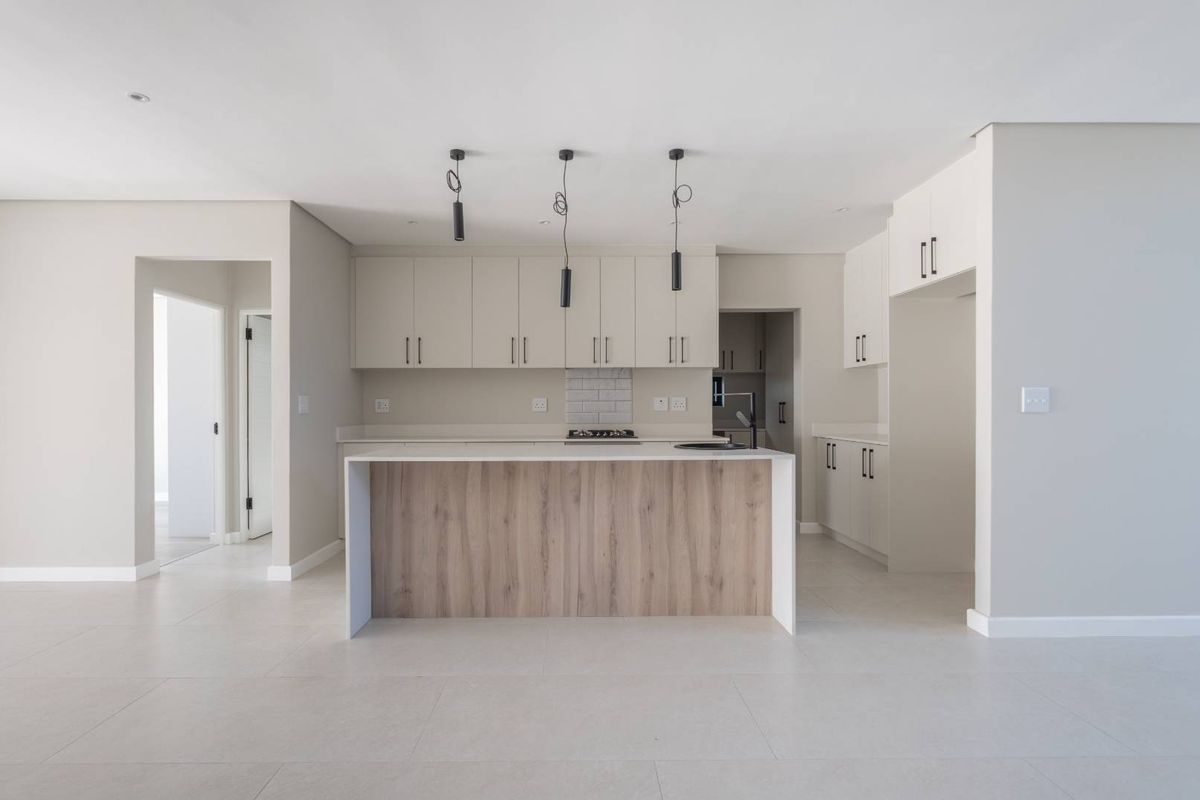 Modern, minimalist kitchen featuring a central island with wood-look finish, stone countertops, built-in cabinetry, and sleek pendant lighting in an open-plan layout.
