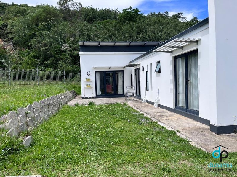 Rear view of the property featuring a concrete patio, sliding glass doors, and a landscaped garden area with a retaining wall.
