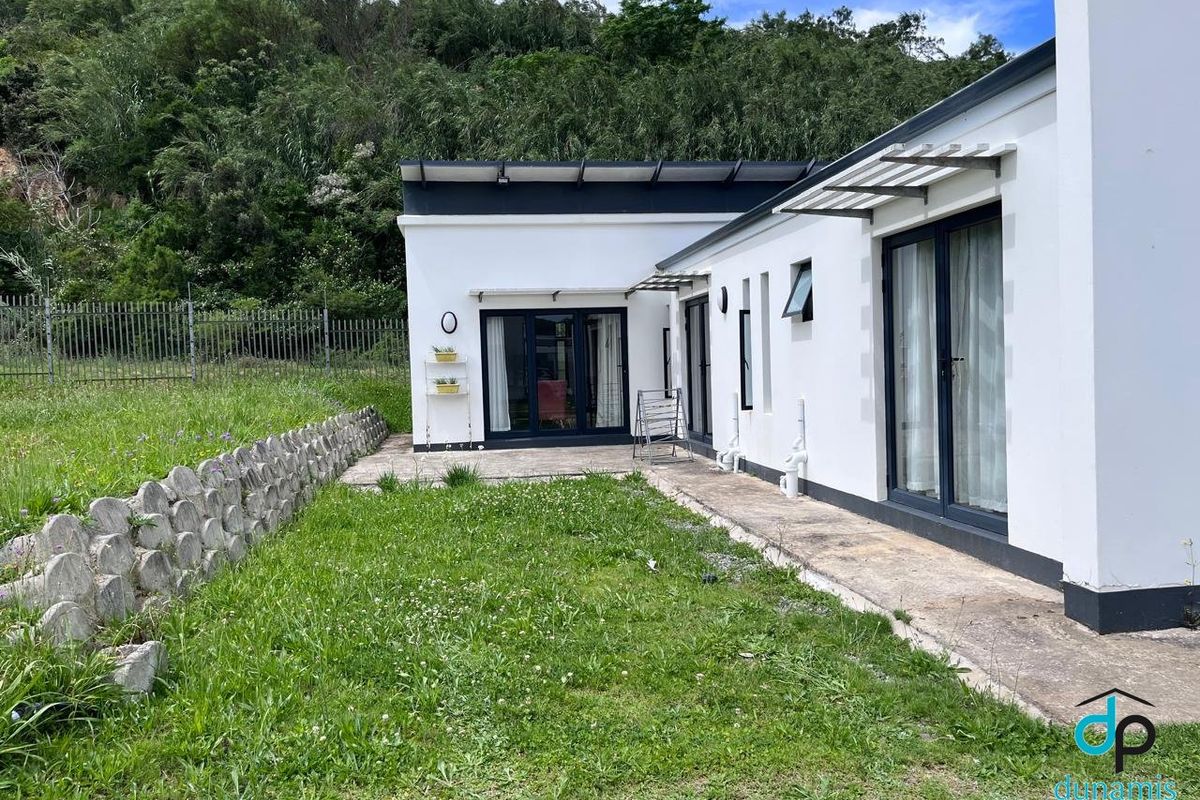 Rear view of the property featuring a concrete patio, sliding glass doors, and a landscaped garden area with a retaining wall.