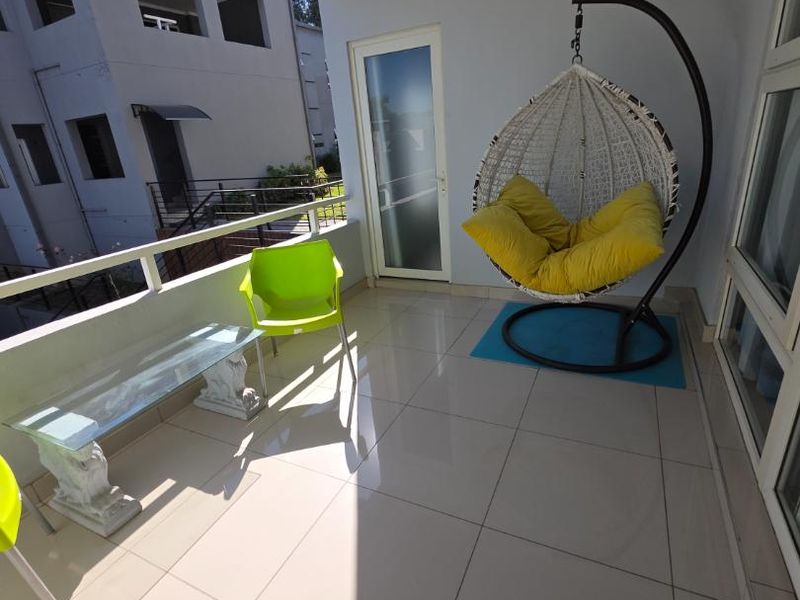 A bright, covered balcony featuring tiled flooring and a metal balustrade, offering a pleasant outdoor space for relaxation.