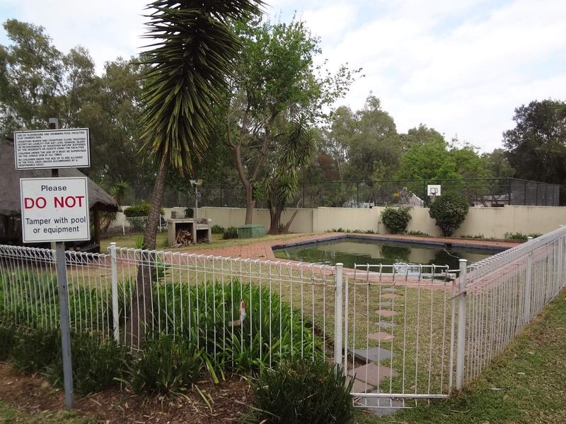 Communal pool area featuring a swimming pool, brick paving, built-in braai, and a thatched lapa, enclosed by perimeter fencing.