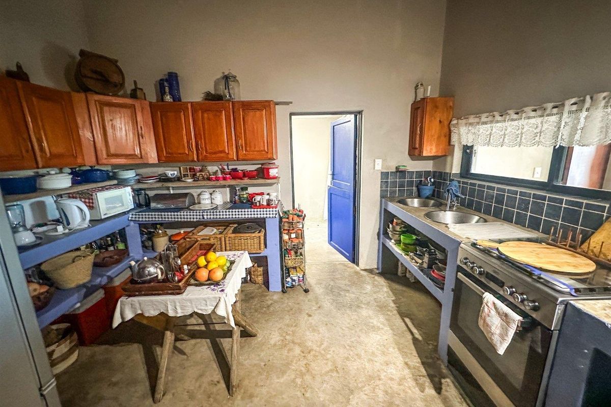 A rustic kitchen featuring built-in cabinetry, a double sink, tiled splashback, and a freestanding oven, with concrete flooring throughout.