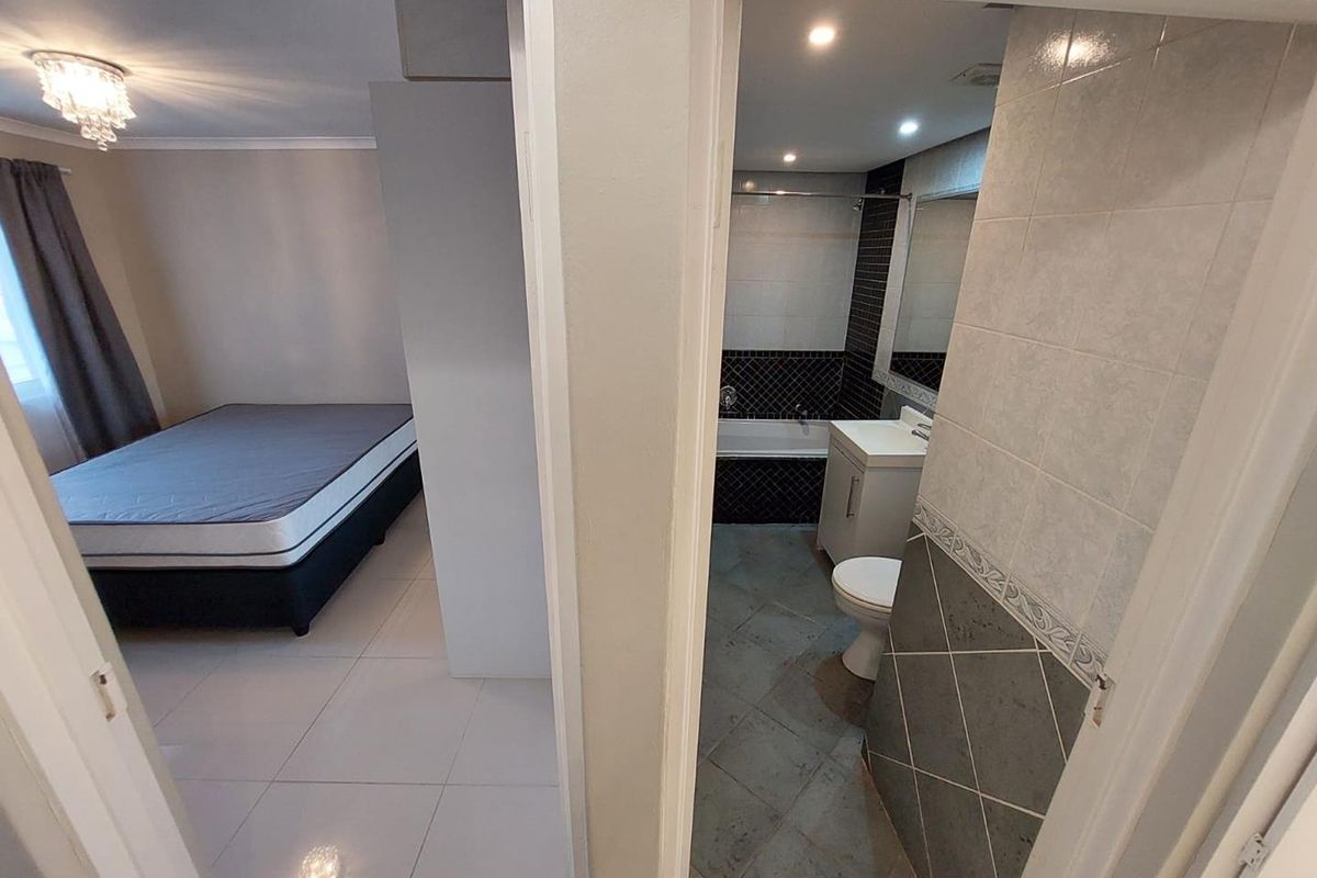 A bedroom featuring tiled flooring and an en-suite bathroom equipped with a vanity and bathtub, showing a functional and clean layout.