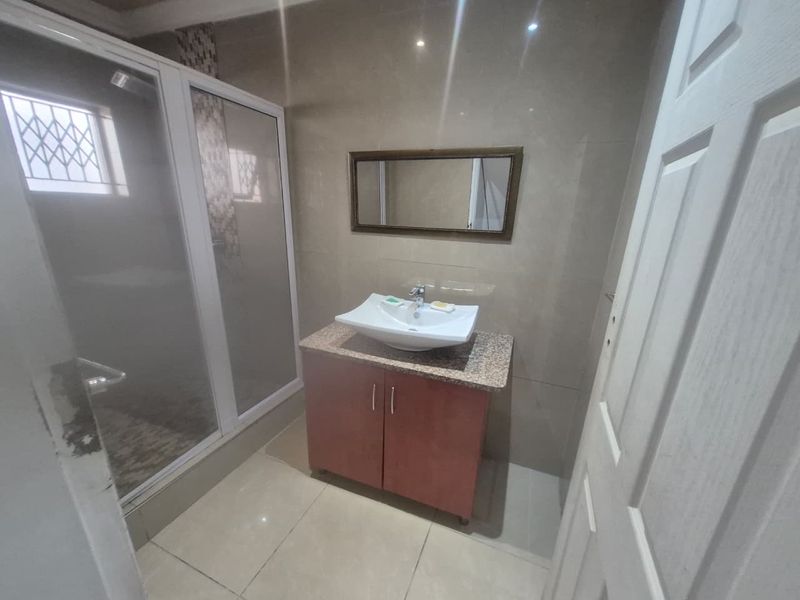 A functional bathroom featuring a vessel sink on a granite-topped vanity, a glass shower enclosure, and neutral wall and floor tiling.