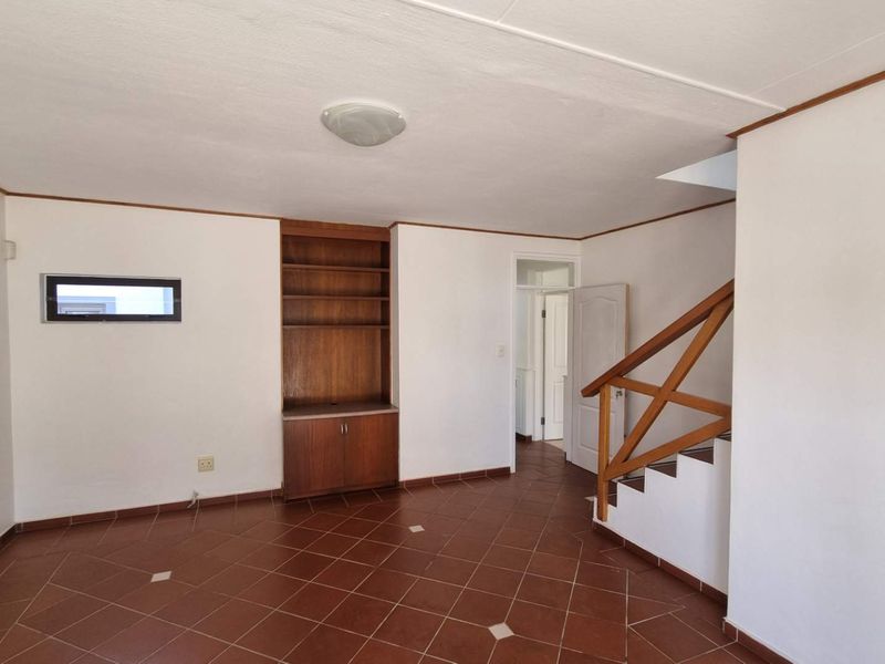 An empty living area featuring tiled flooring, a built-in wooden storage unit, and a staircase with a wooden handrail.