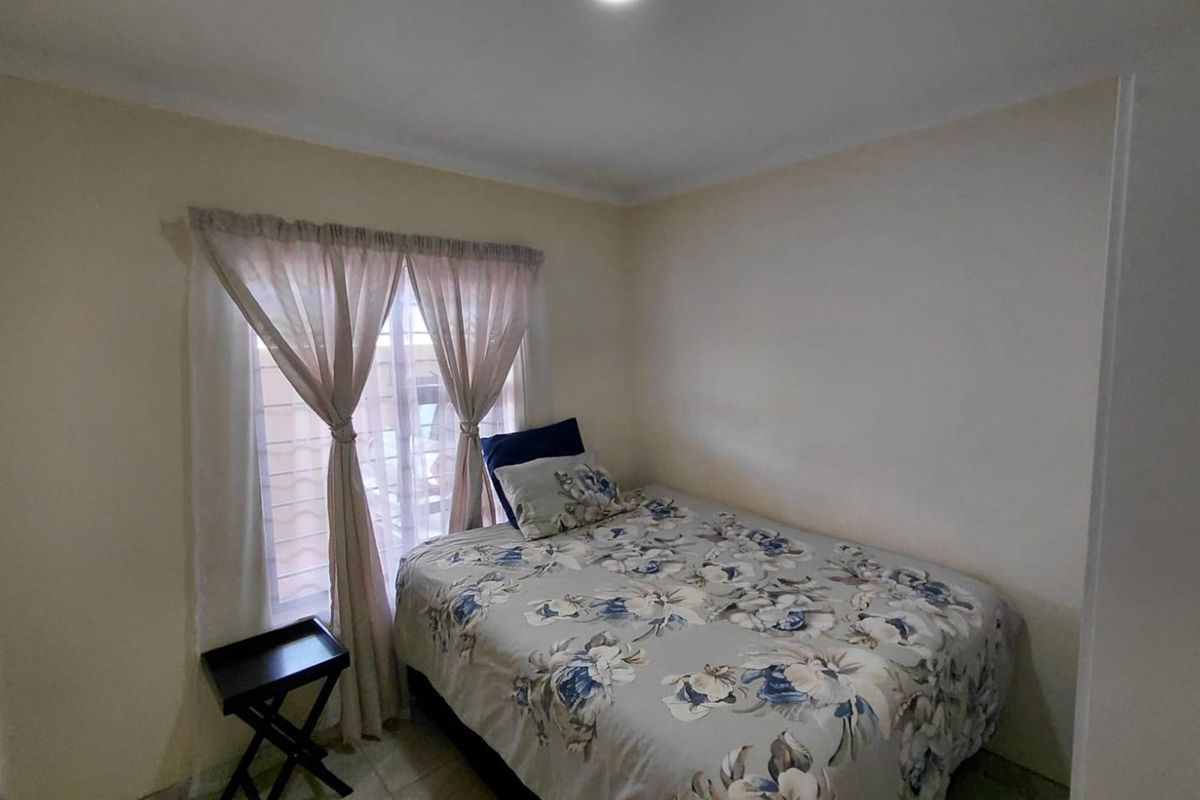 A functional bedroom featuring tiled flooring, neutral wall finishes, and a window with fitted curtain tracks.