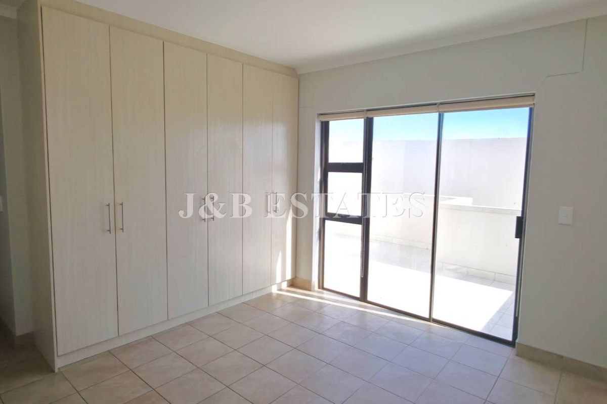 A bright bedroom featuring built-in cupboards, tiled flooring, and sliding glass doors providing access to an outdoor balcony area.