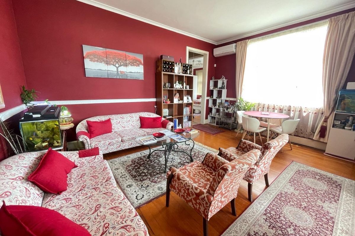 A spacious living room featuring hardwood flooring, chair rail molding, and a wall-mounted split-system air conditioner, with ample natural light from a large window.