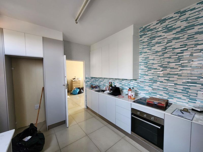 Modern kitchen featuring white cabinetry, a striking blue and white mosaic tile backsplash, built-in oven, electric hob, and tiled flooring.