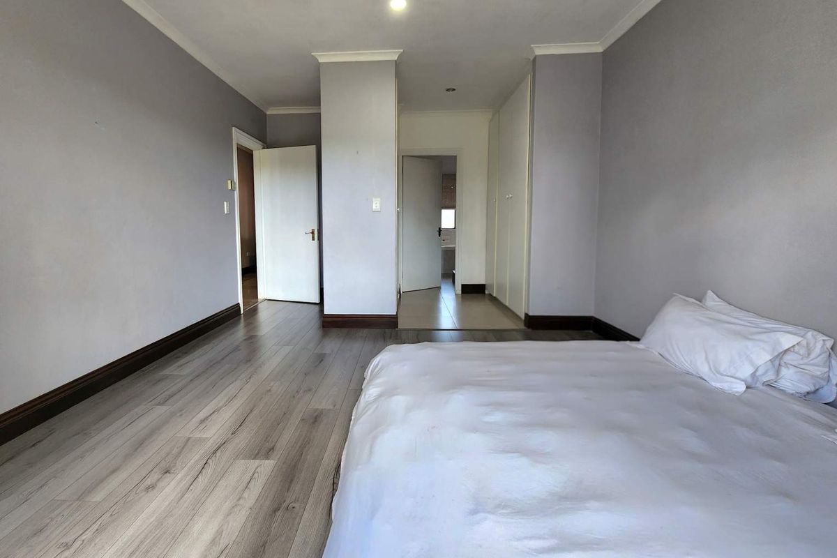 Spacious bedroom featuring light wood-look laminate flooring, built-in cupboards, and neutral wall tones, with direct access to an adjoining room.