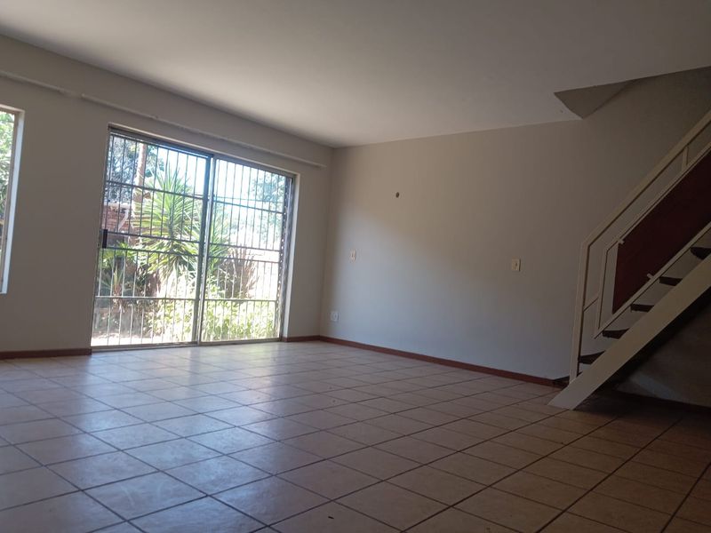 An empty, open-plan living area featuring tiled flooring, a staircase, and a sliding glass door with security bars leading to the exterior.