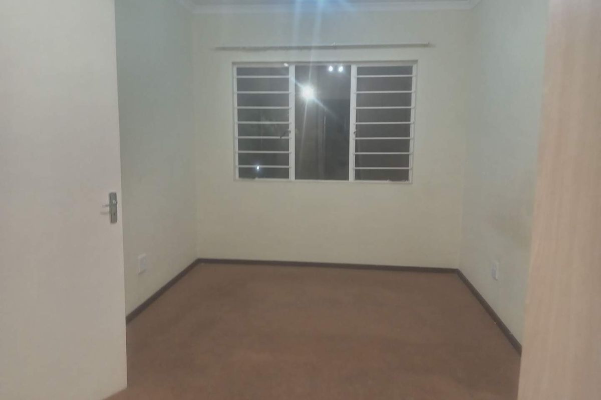 A vacant bedroom featuring neutral walls, carpeted flooring, and a window fitted with security bars.