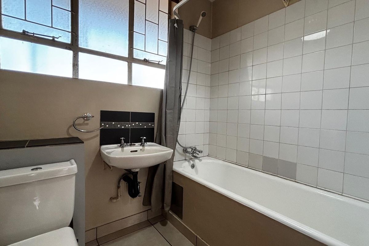 A functional bathroom featuring a standard bathtub with shower attachment, wall-mounted basin, and toilet, finished with white wall tiles and neutral paint.