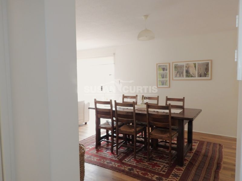 A dining area featuring laminate flooring and a central pendant light fixture, viewed from an adjacent room.